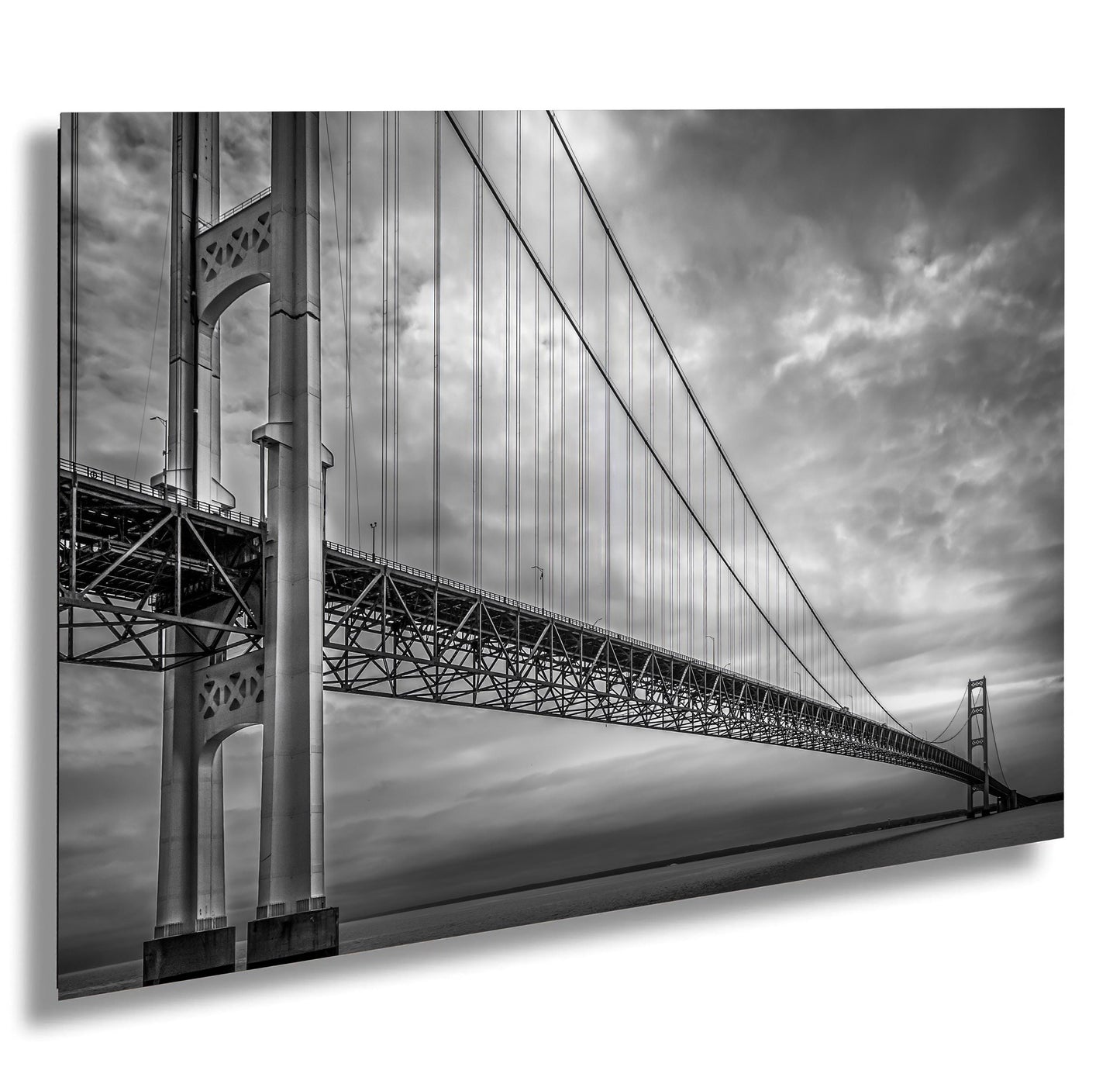 A black and white photograph of the Mackinac Bridge, capturing the engineering and grandeur of the structure with a backdrop of overcast sky and a body of water.