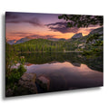 a serene lake surrounded by a forested mountain range, with the sky painted in warm hues of orange and pink, creating a picturesque and tranquil scene.