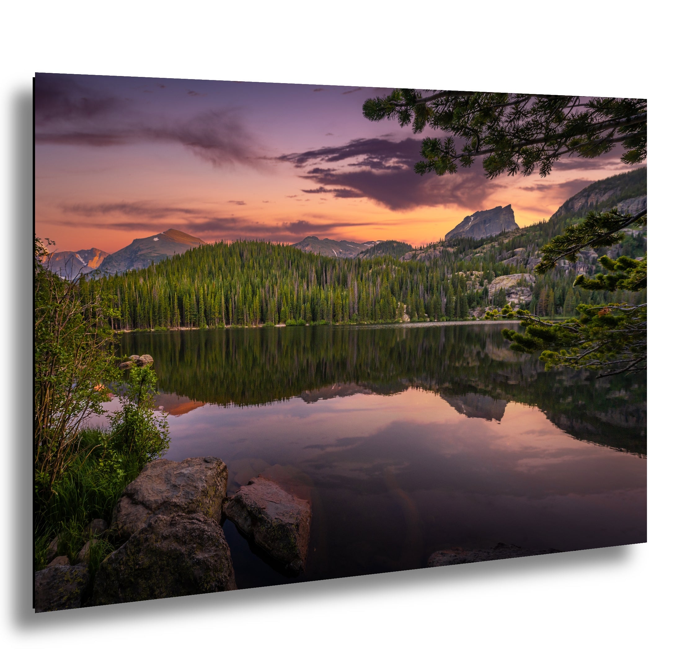 a serene lake surrounded by a forested mountain range, with the sky painted in warm hues of orange and pink, creating a picturesque and tranquil scene.