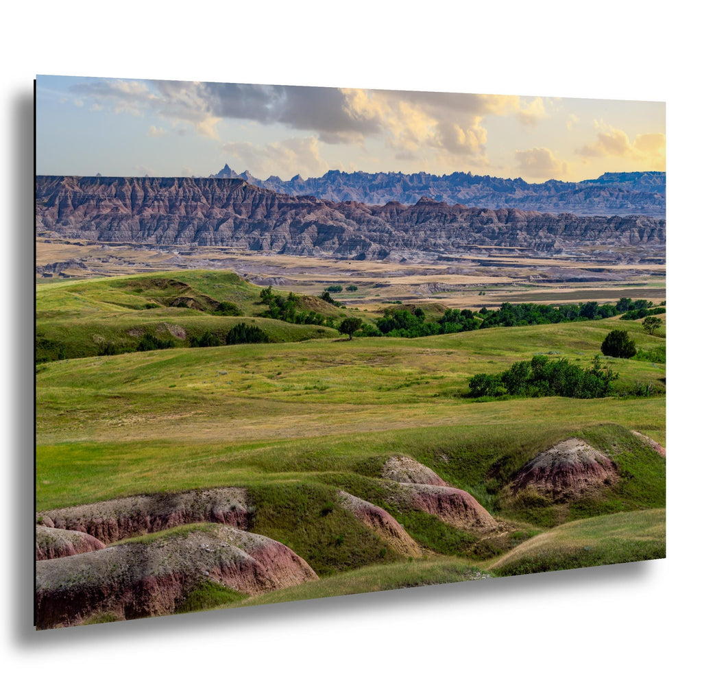 Badlands prairie with green hills and banded buttes beneath soft clouds, South Dakota landscape