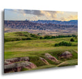 Badlands prairie with green hills and banded buttes beneath soft clouds, South Dakota landscape