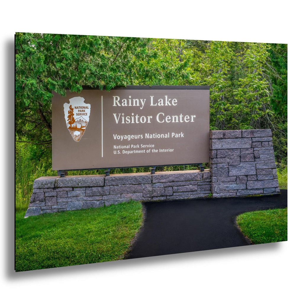 Rainy Lake Visitor Center sign at Voyagers National Park with stone structure and greenery.