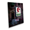 A vibrant night photograph of the "The Redhead Piano Bar" neon sign featuring a winking redhead woman, displayed as a metal or acrylic print mockup against a dark brick urban building background.
