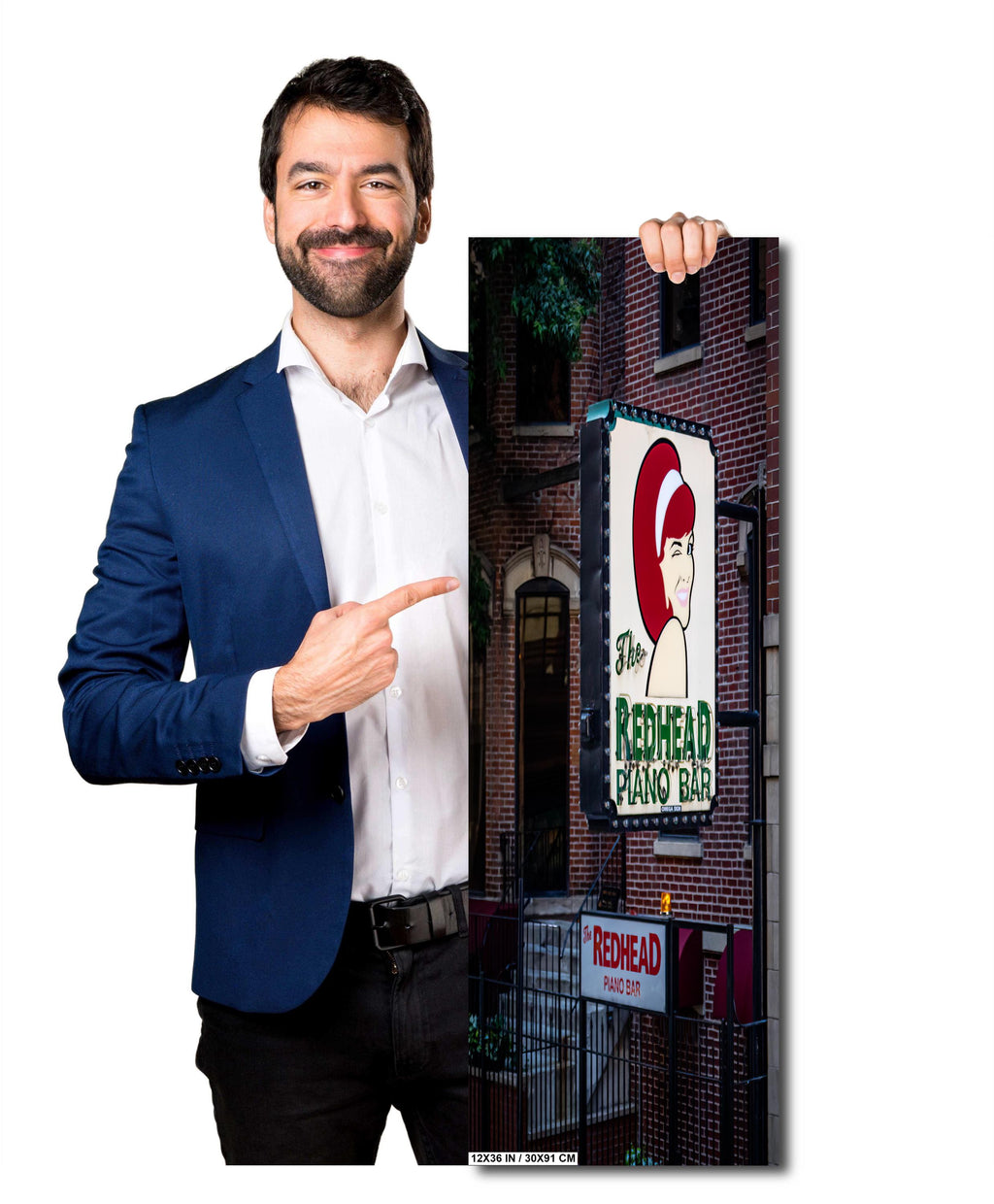 A man holding a 16x20 inch portrait-oriented photo print of "The Redhead Piano Bar" neon sign against a solid light grey background.