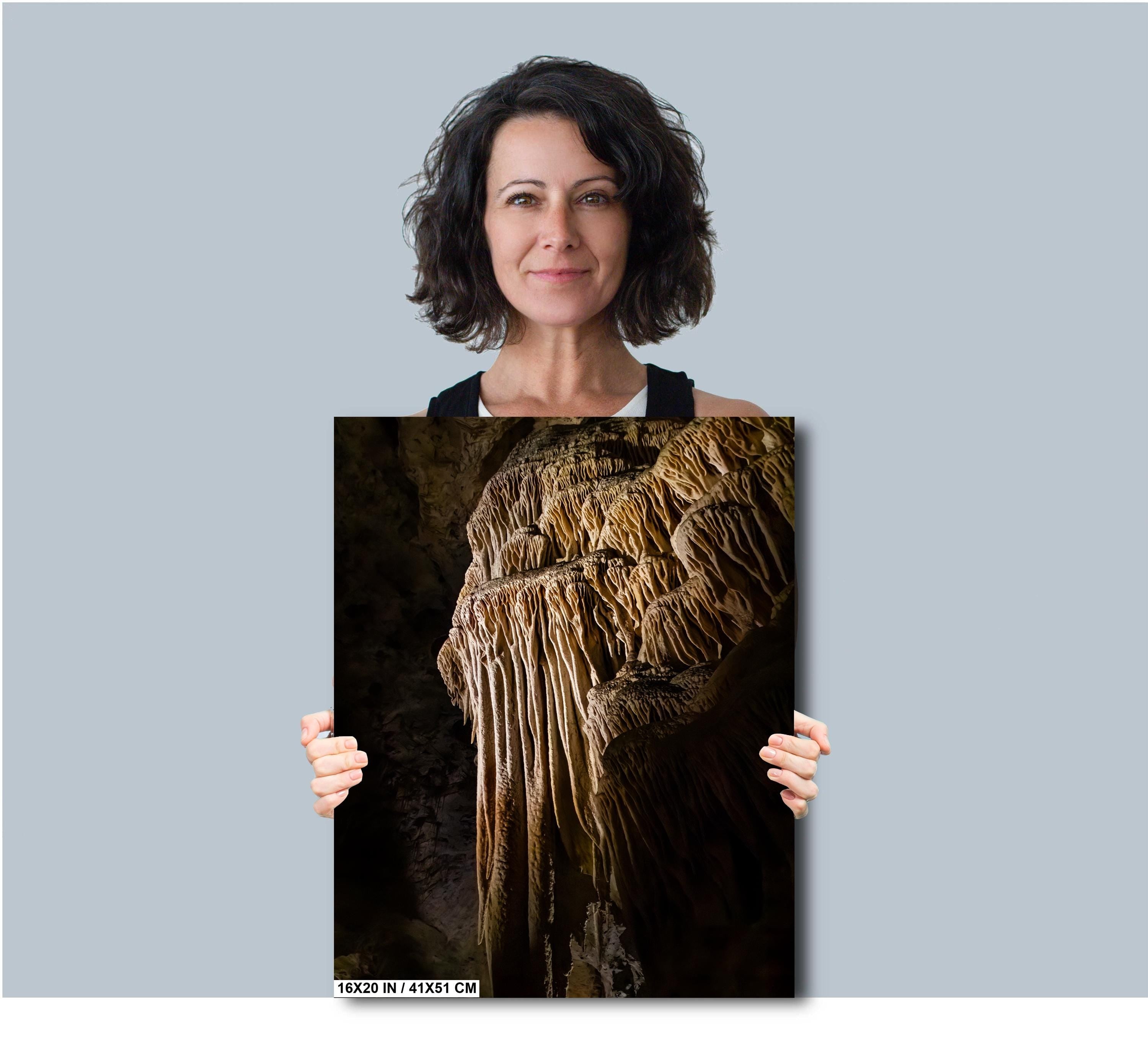 A woman holding a 16x20 inch (41 x 51 cm) portrait-oriented art print of a golden-brown limestone stalactite formation against a solid light grey background.