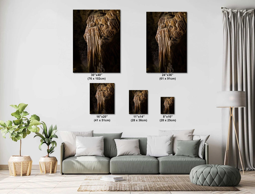 A living room size chart featuring five different portrait-oriented art prints of a golden-brown limestone stalactite formation, ranging in size from 8x10 inches to 30x40 inches, displayed on a white wall above a modern grey sectional sofa.