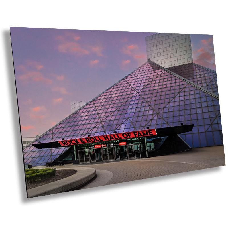A print of the Rock and Roll Hall of Fame museum in Cleveland, Ohio, featuring the glass pyramid structure with a pink and blue sky backdrop.