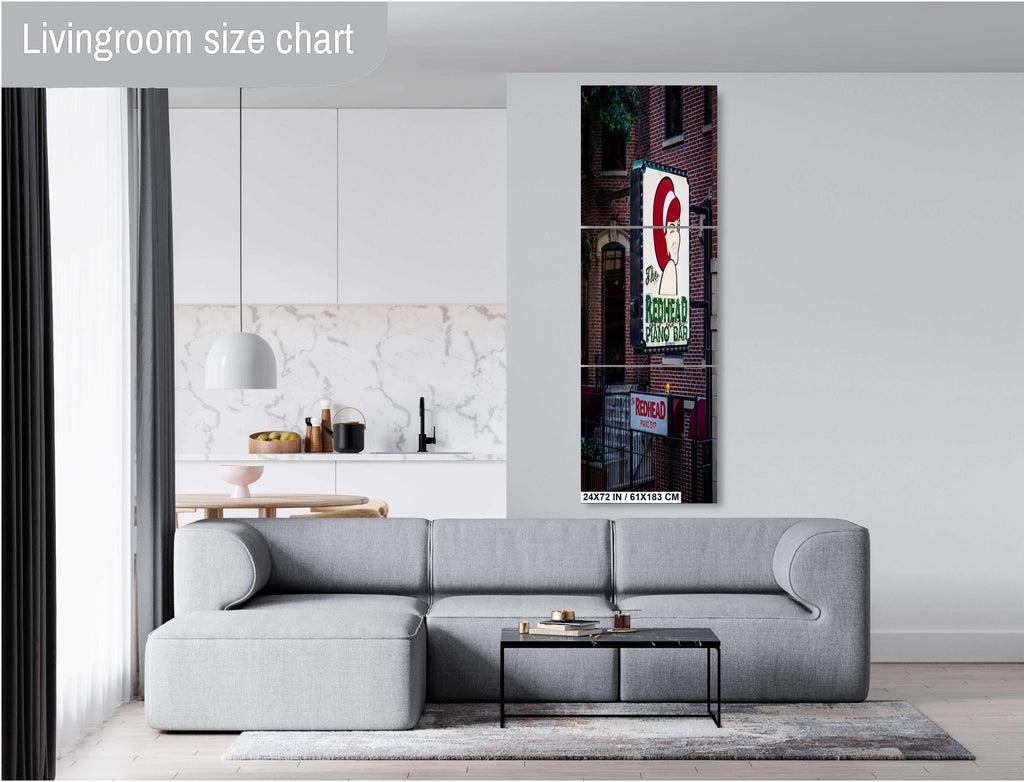 A three-panel vertical triptych art print of "The Redhead Piano Bar" neon sign, measuring 24 x72 inches, mounted on a light grey wall above a modern grey sectional sofa in a bright living room with a view of a kitchen.