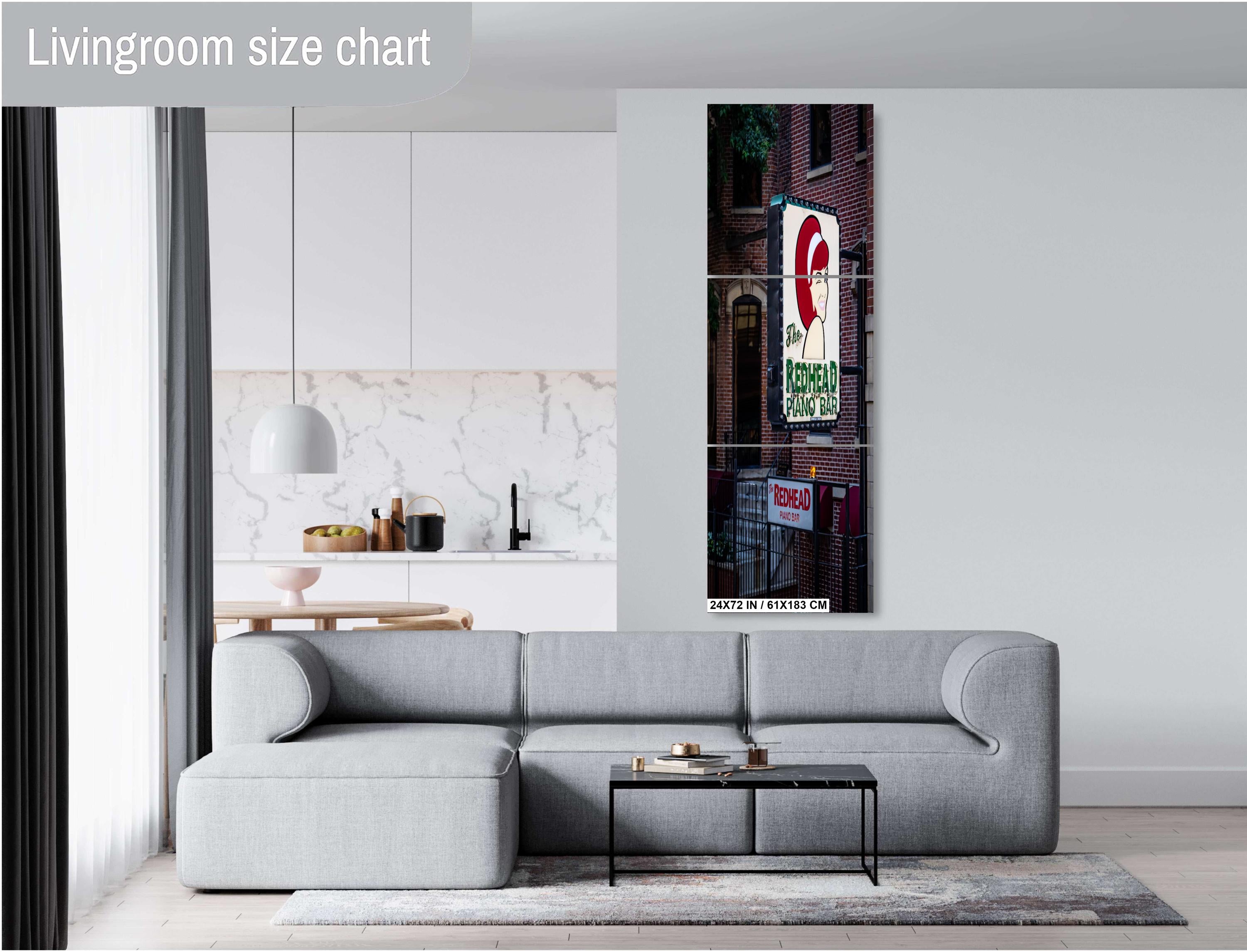 A three-panel vertical triptych art print of "The Redhead Piano Bar" neon sign, measuring 24 x72 inches, mounted on a light grey wall above a modern grey sectional sofa in a bright living room with a view of a kitchen.