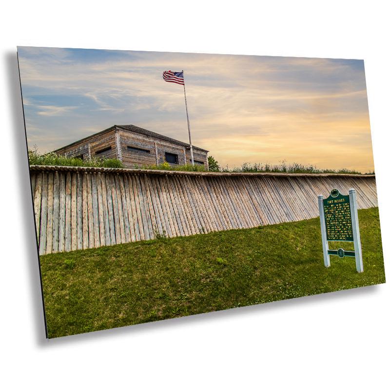 A historical marker sign featuring the Fort Holmes sign with a background of a wooden fence and a flag, capturing a moment of history on Mackinac Island.